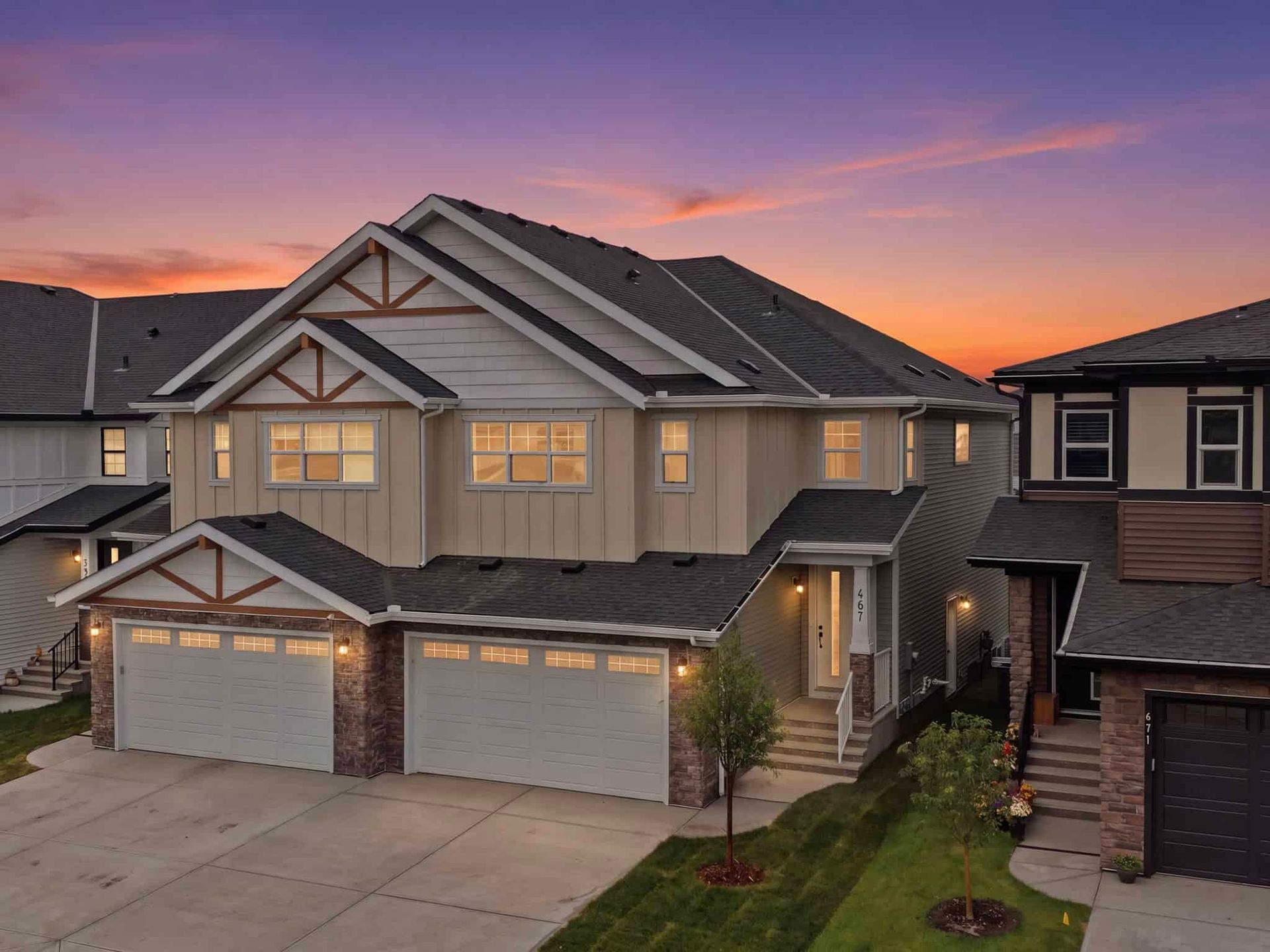 Row of modern townhouses with attached garages and gabled roofs at sunset, windows lit.
